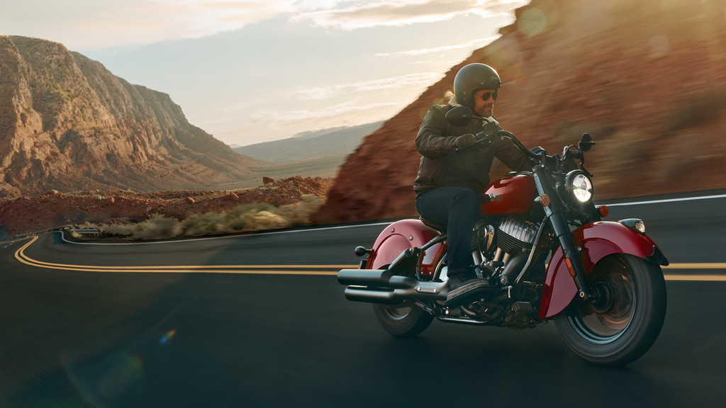 Rider on a red Indian Chief Vintage motorcycle traveling through a sunlit canyon